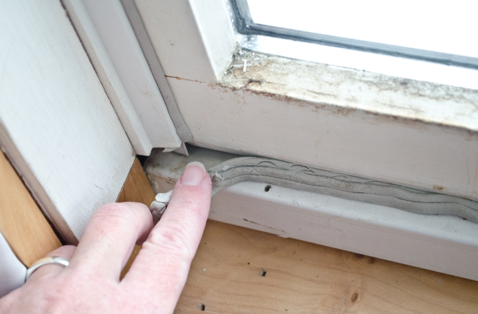 Woman's hand pulling back loose caulking causing heat loss