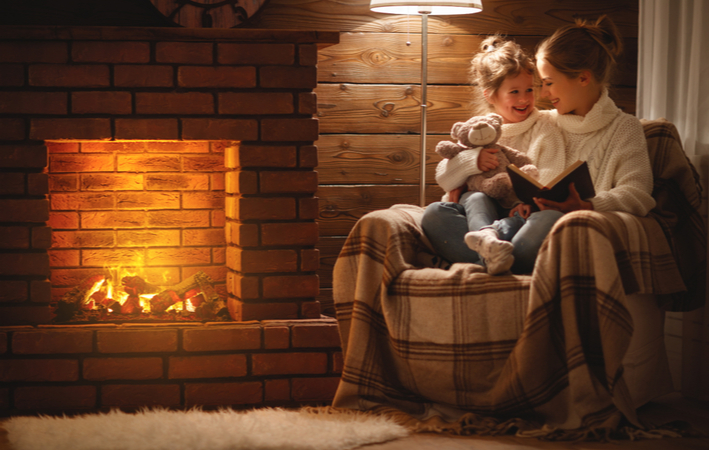 mother and daughter reading a book in front of a fireplace