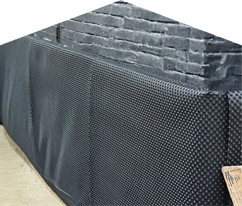 Exterior basement waterproofing completed by Dunn, showing a sealed foundation wall with dimpled waterproof membrane partially installed on a brick surface, preventing moisture infiltration.