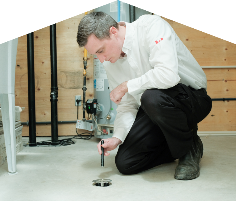 Dunn plumbing specialist inspecting a basement floor drain with a flashlight during a drain cleaning service, in a utility room with visible pipes, water heater, and wood panel walls. Dunn plumbing specialist inspecting a basement floor drain with a flashlight during a drain cleaning service, in a utility room with visible pipes, water heater, and wood panel walls.