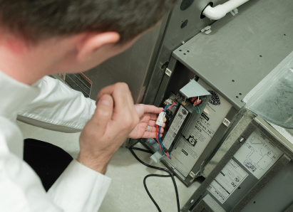 A Dunn heating technician inspecting internal wiring during a service check on a residential heating unit. A Dunn heating technician inspecting internal wiring during a service check on a residential heating unit.