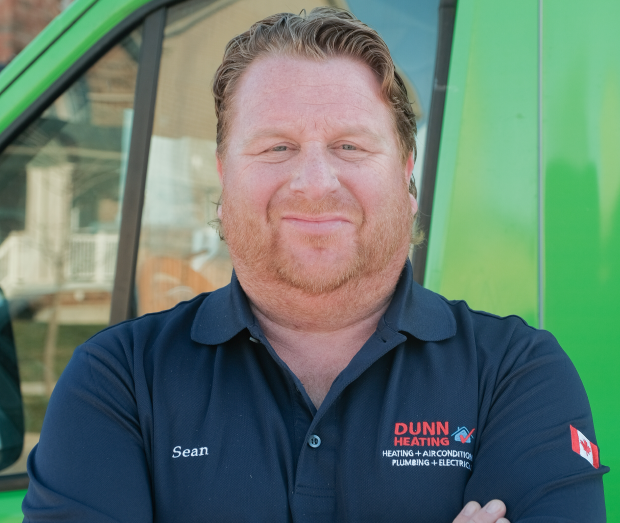 Smiling Dunn technician standing confidently in front of their green service van, wearing their white issued uniform. Smiling Dunn technician standing confidently in front of their green service van, wearing their white issued uniform.